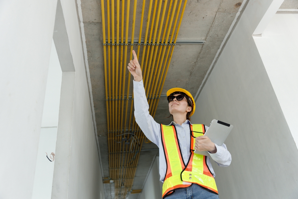 Female,Construction,Engineer,Pointing,At,Overhead,Electrical,Conduits,During,Site