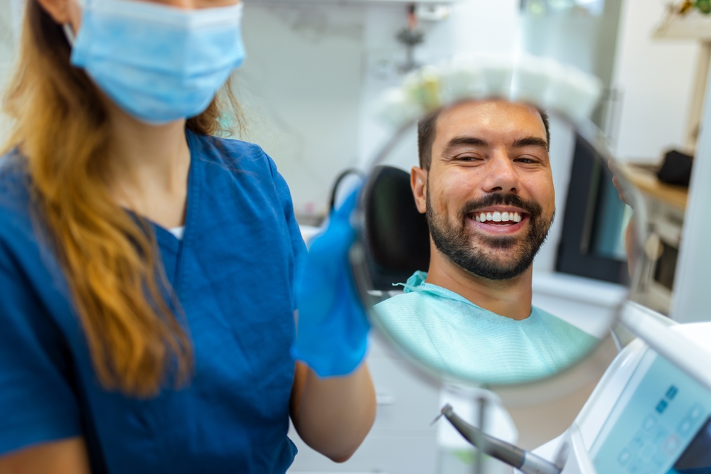 Female,Dentist,Helping,Male,Patient,See,His,Smile,Using,A